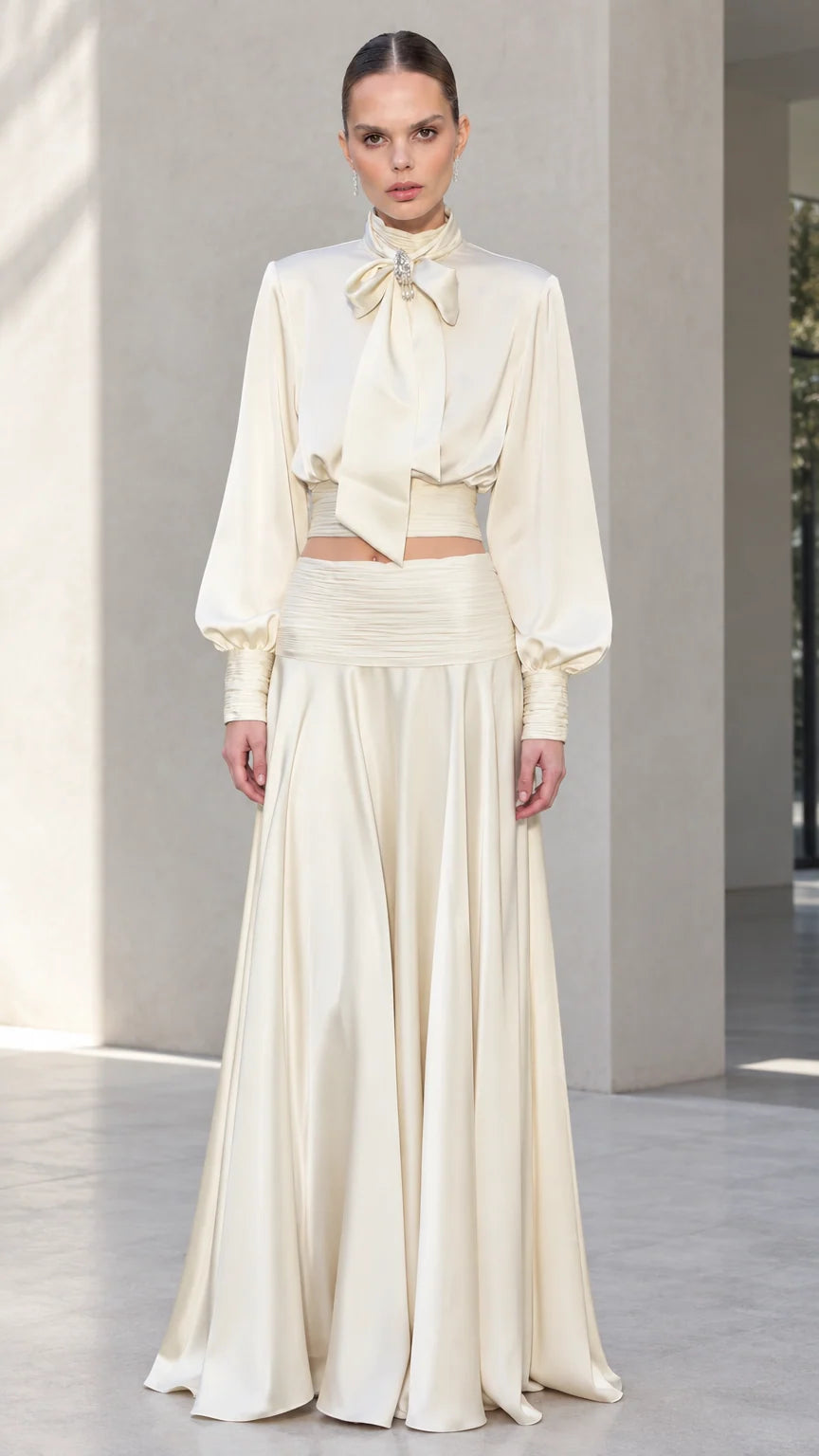 Front view of model wearing ivory satin bow tie blouse and matching pleated maxi skirt set