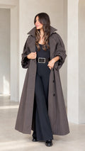 Front full view of woman wearing charcoal brown maxi trench coat with volume sleeves