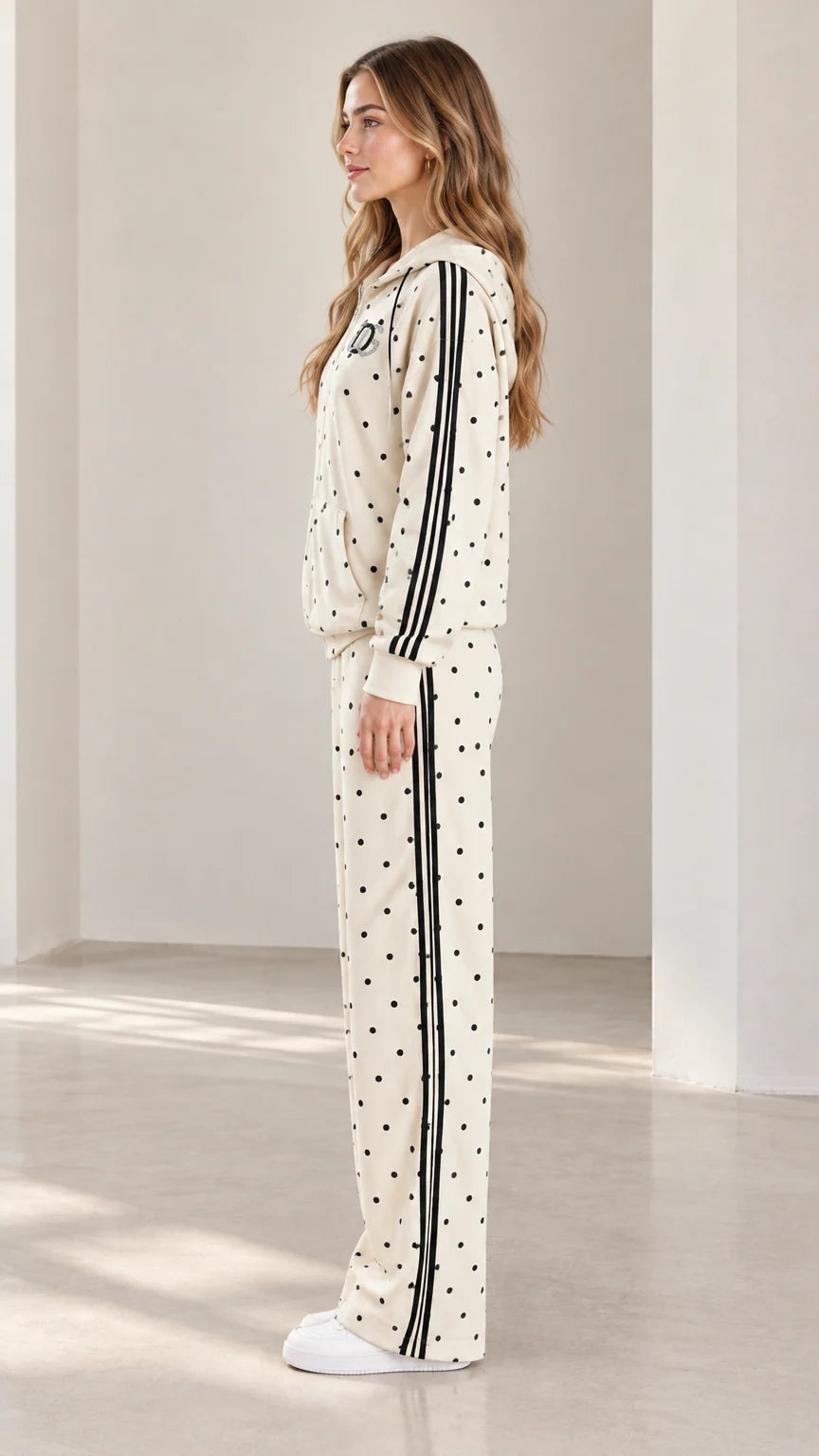 Side profile view of model showcasing black side stripes on cream polka dot tracksuit