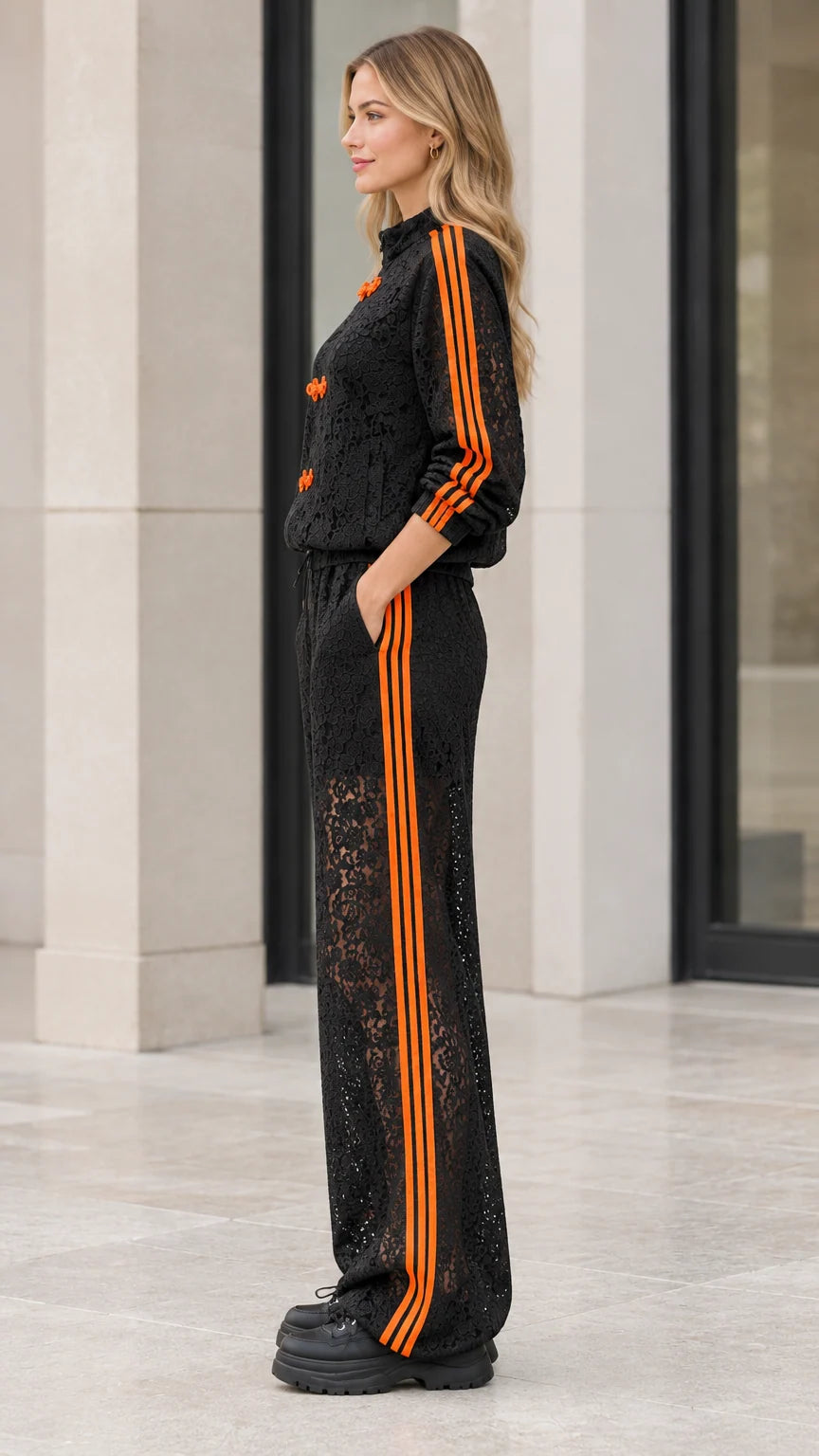 Side profile view of woman wearing black lace tracksuit with orange sleeve and pant stripes