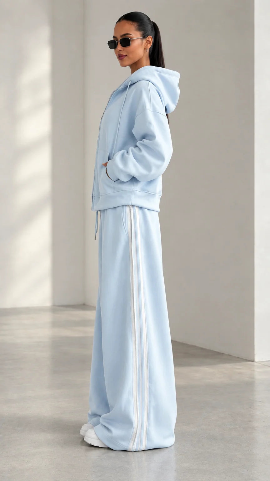 Side angle view of model wearing Light Blue two-piece tracksuit with white side stripes