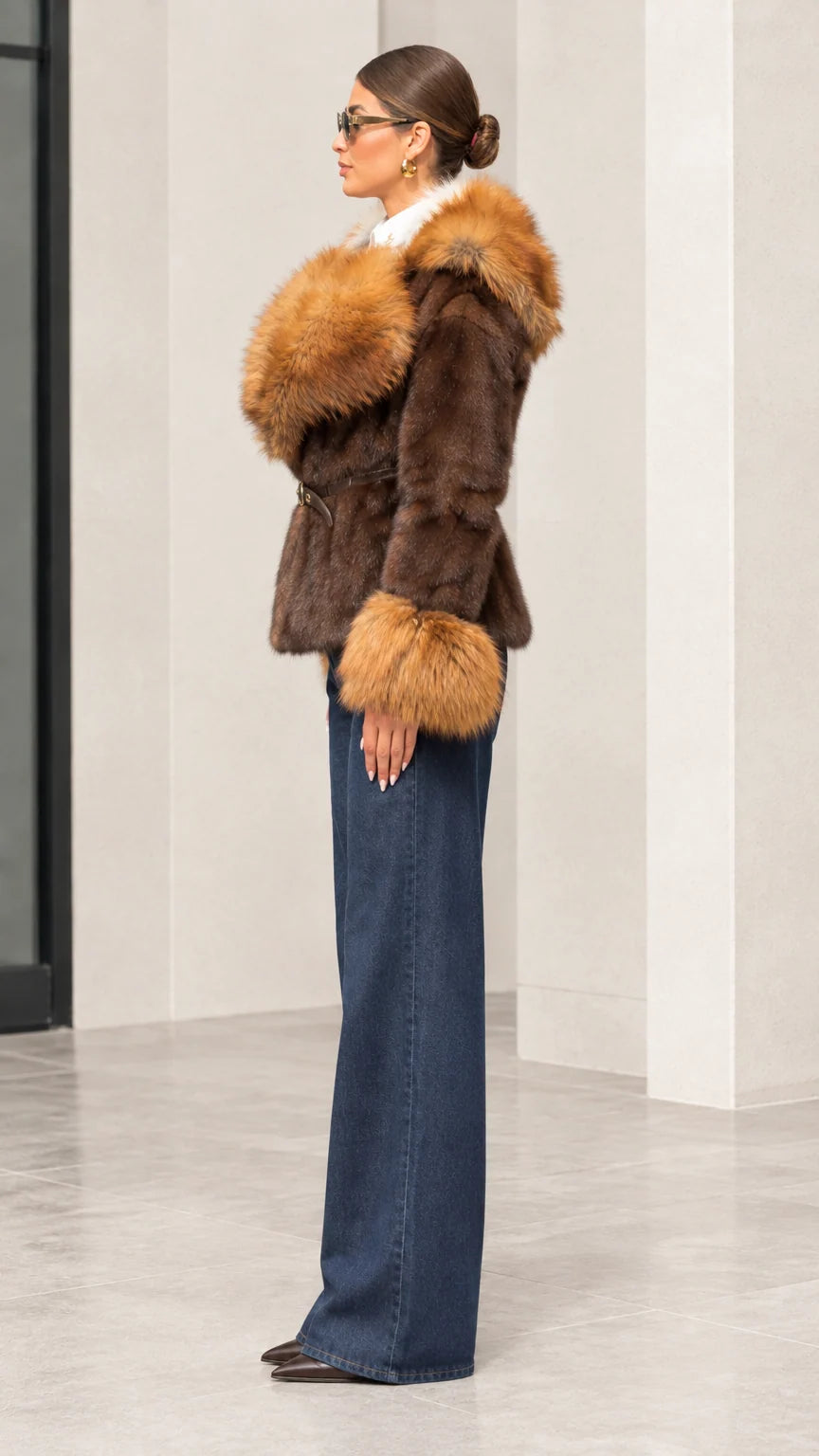 Side profile view of woman modeling brown faux fur trim hooded jacket paired with wide-leg jeans