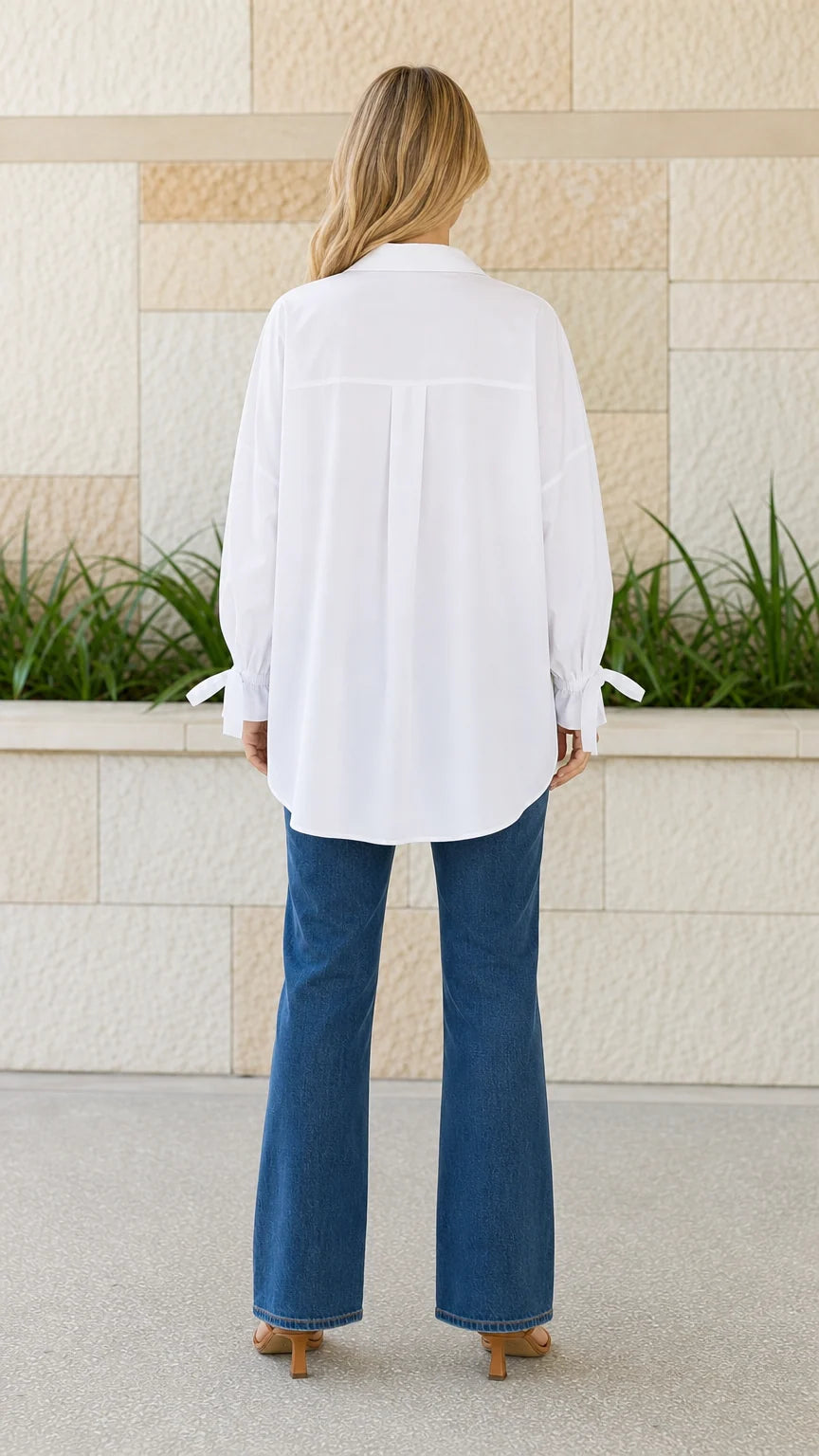 Back view of woman wearing white oversized button-down shirt with curved hem
