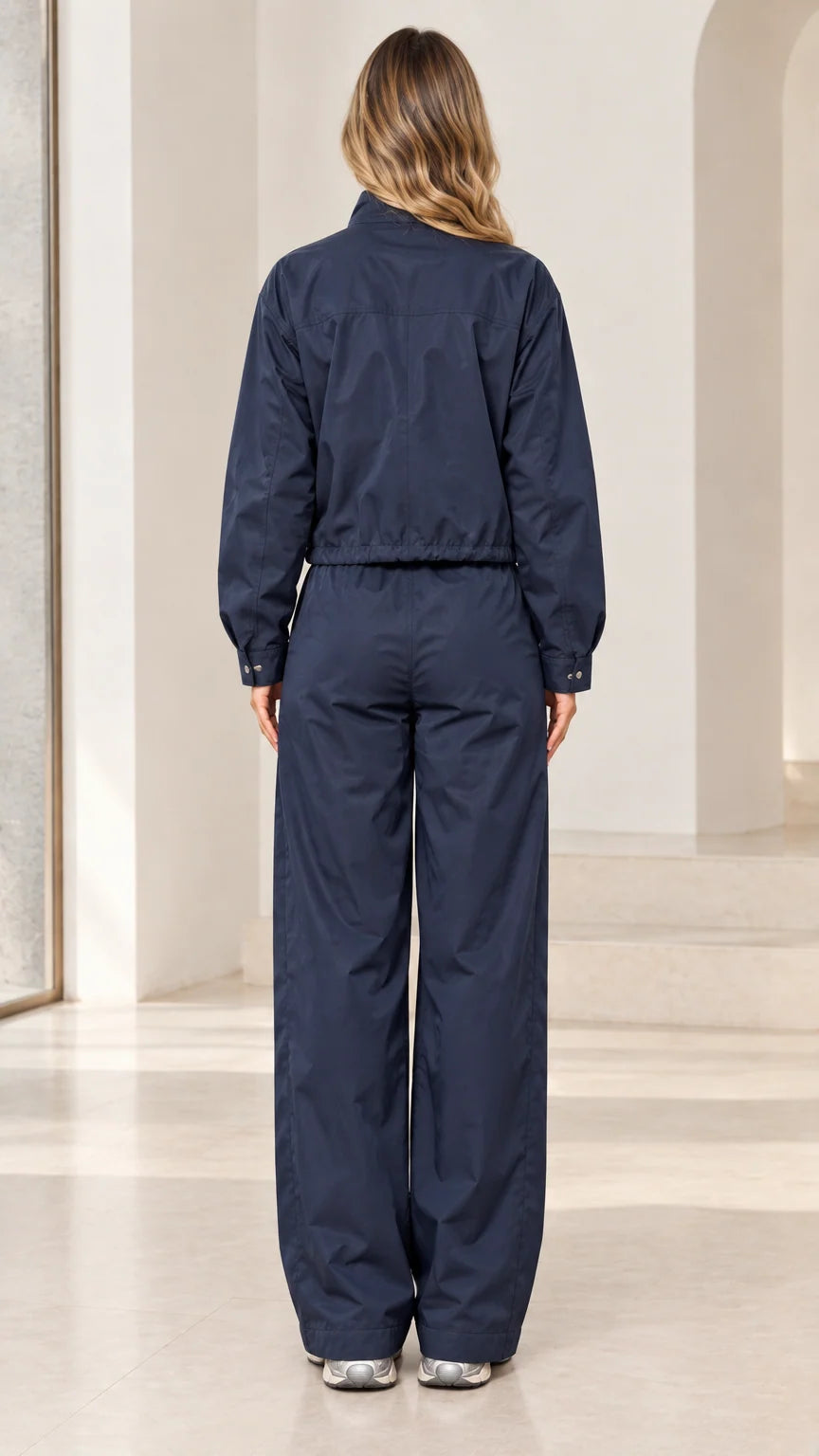 Back full-length view of woman wearing navy blue track jacket and wide-leg pants