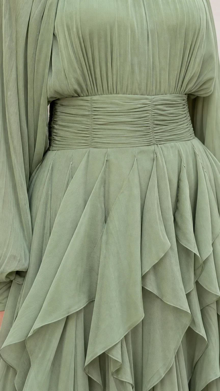 Close-up detail of ruched waistband and layered ruffles on sage green dress