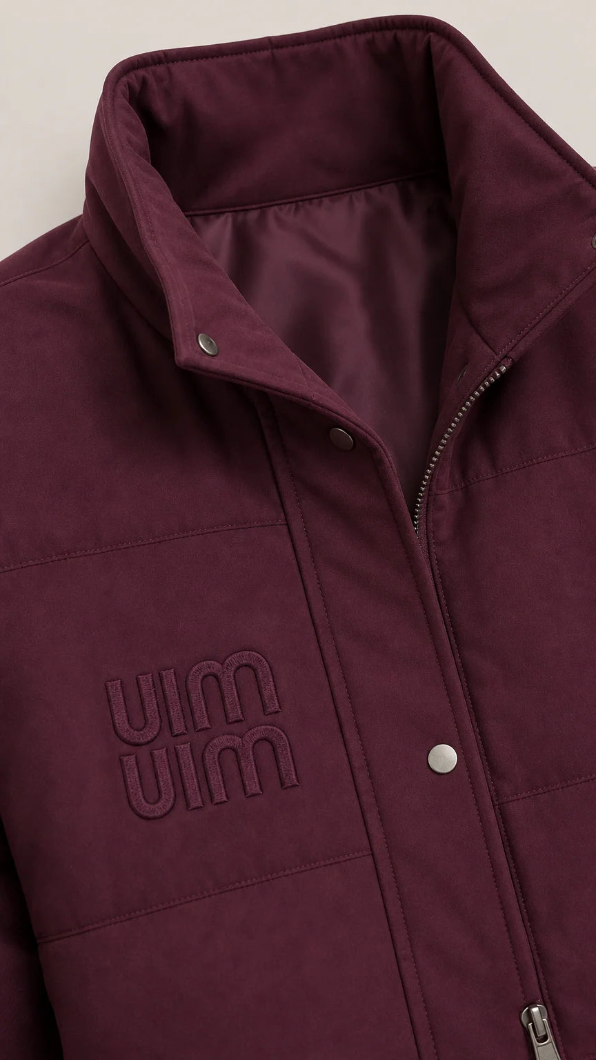 Close-up detail of burgundy stand-collar puffer vest with snap buttons, zipper, and subtle chest embroidery