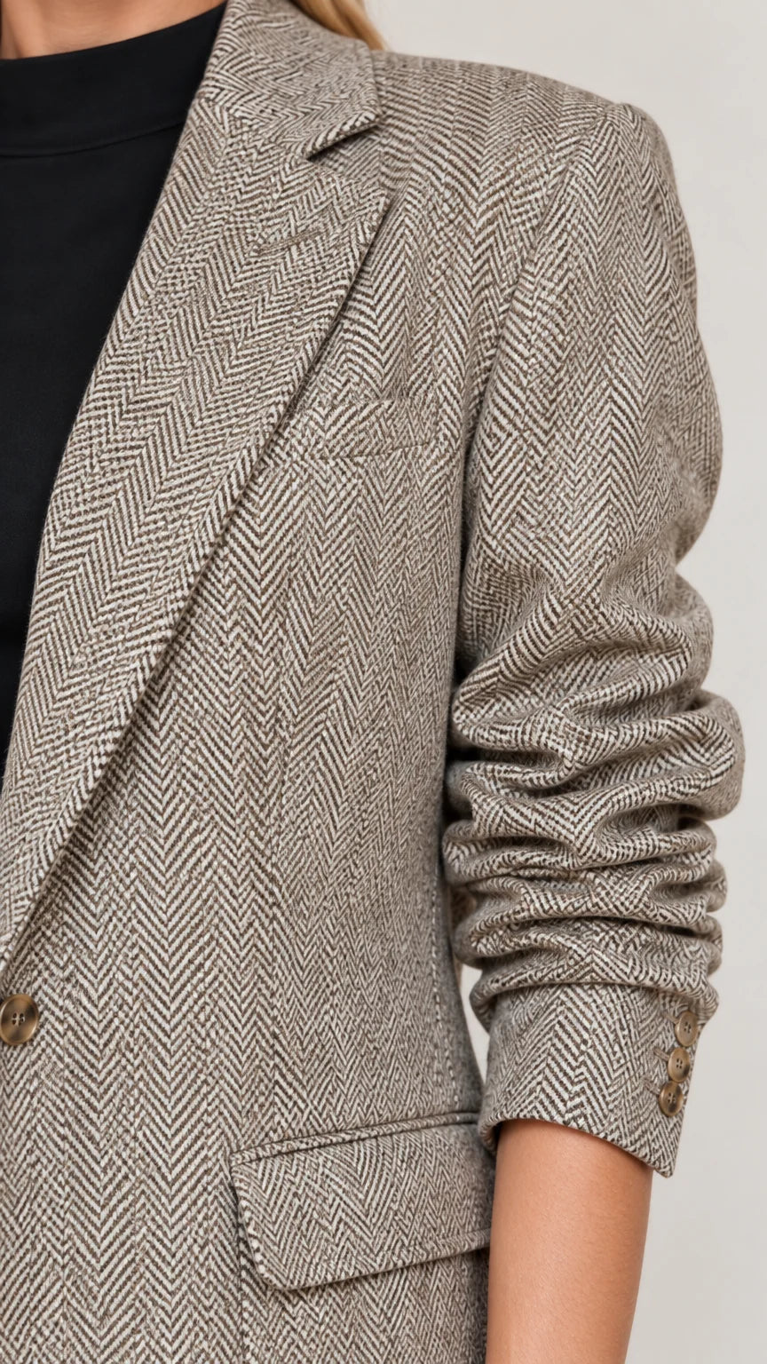 Close-up detail of herringbone textured fabric, notched lapel, and flap pocket
