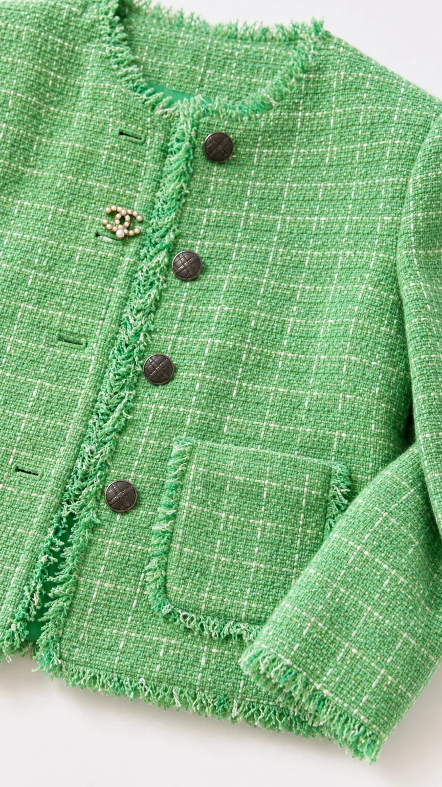 Close-up detail of green tweed fabric, fringe trim, and buttons