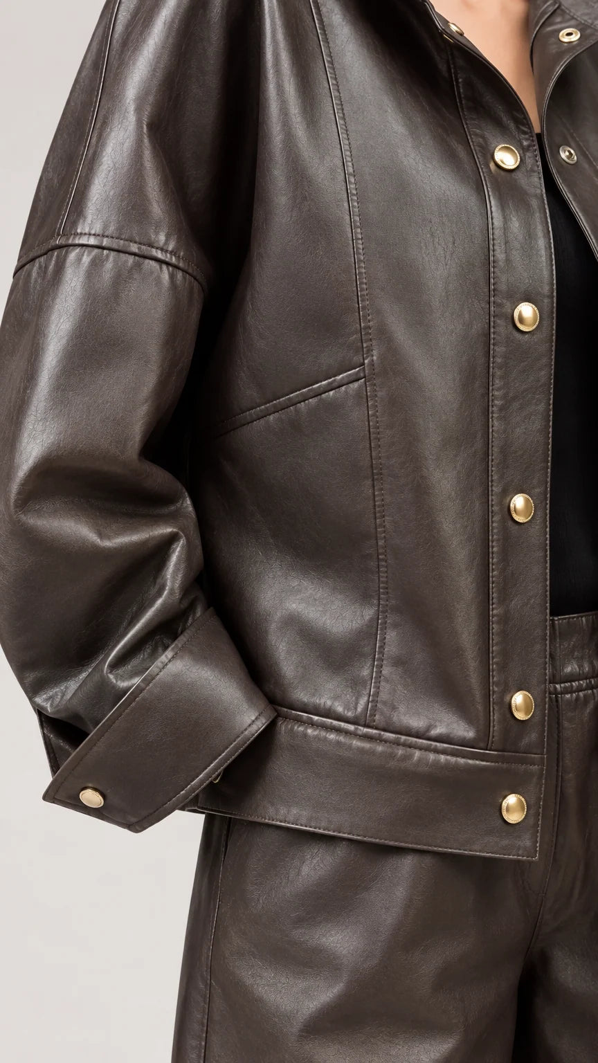Close-up detail of dark brown faux leather jacket with snap buttons and tailored seam lines