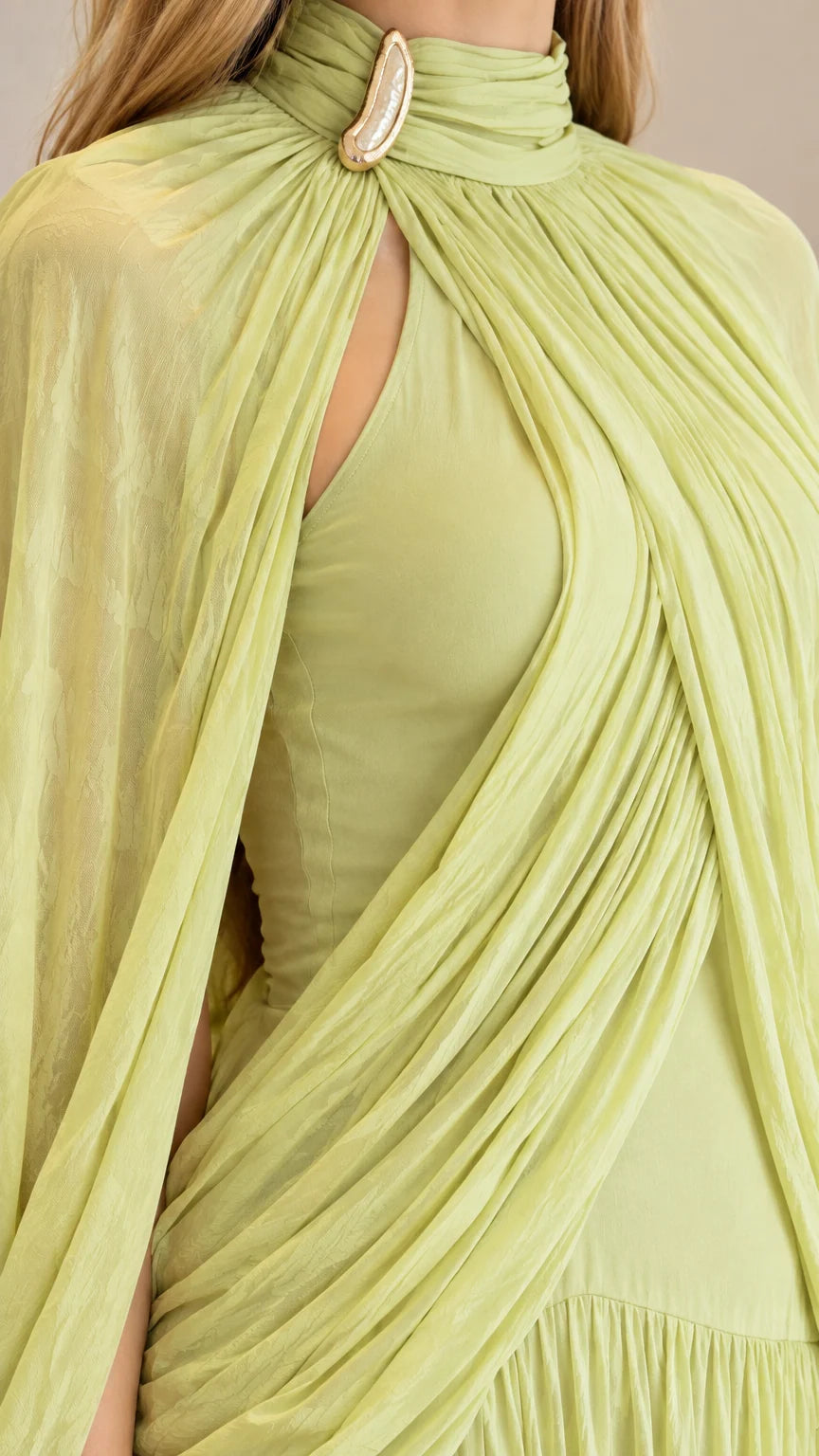 Close-up detail of high neckline, teardrop keyhole, brooch accent, and draped bodice