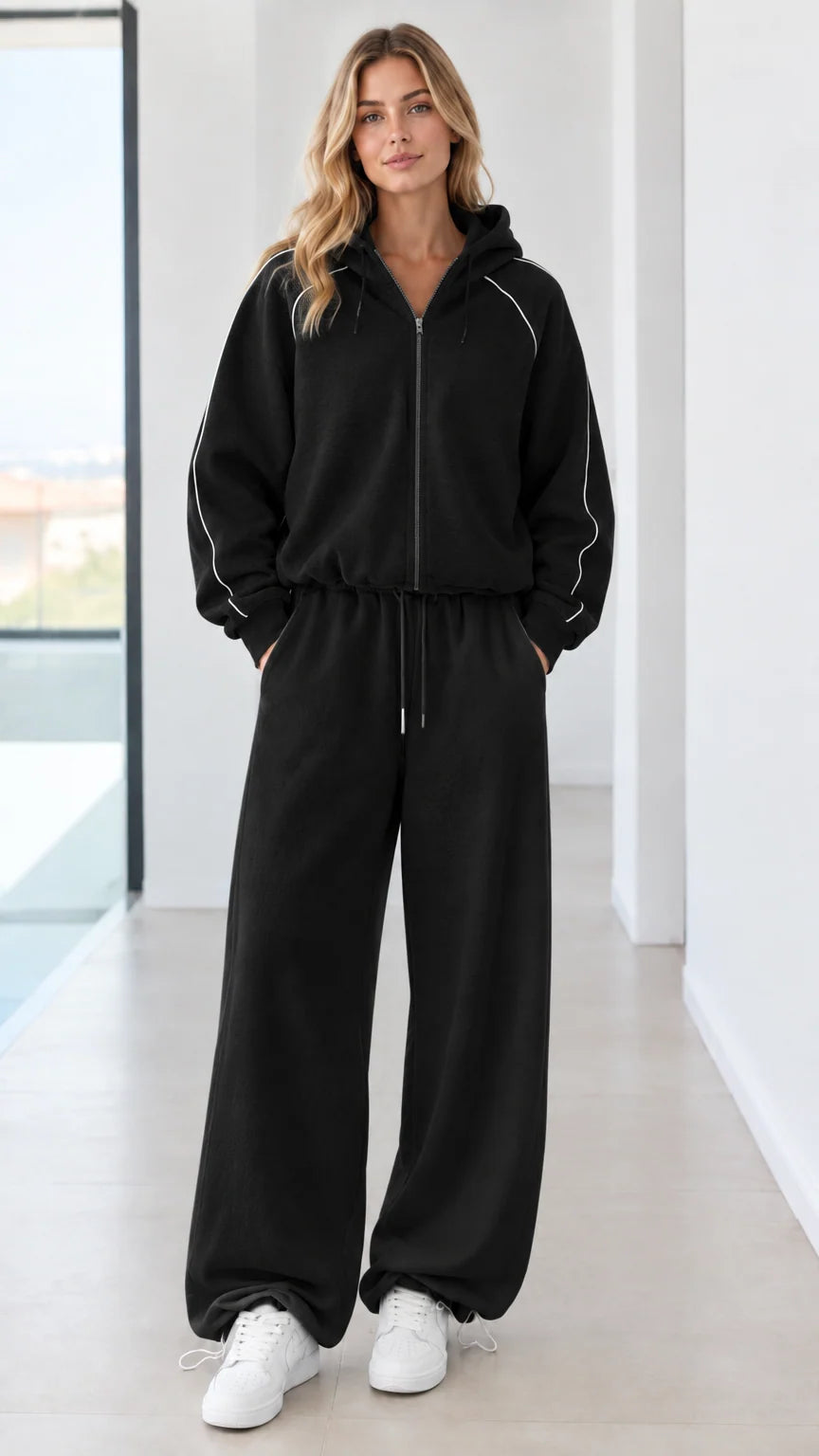 Full body studio shot of model wearing black zip-up hoodie and matching wide-leg sweatpants