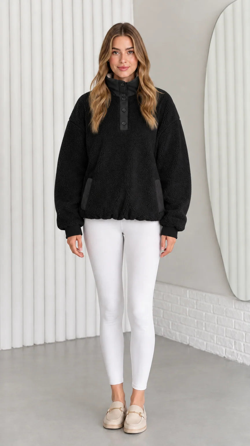Model wearing black sherpa fleece pullover with red cuff accents and white pants