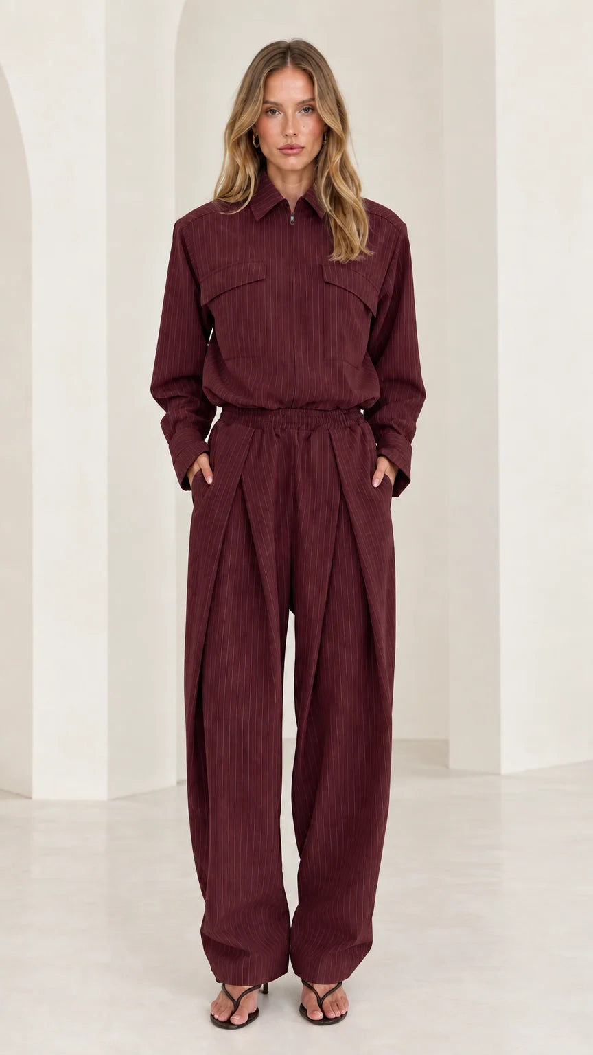 Front view of model wearing burgundy long sleeve pleated wide-leg jumpsuit