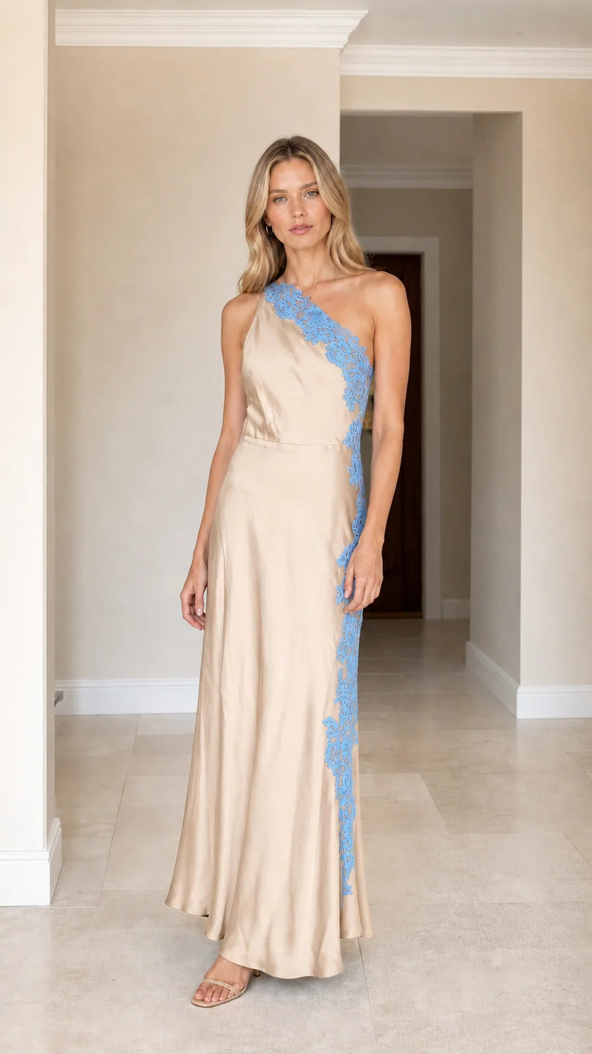 Front view of woman wearing champagne one-shoulder satin maxi dress with blue lace applique