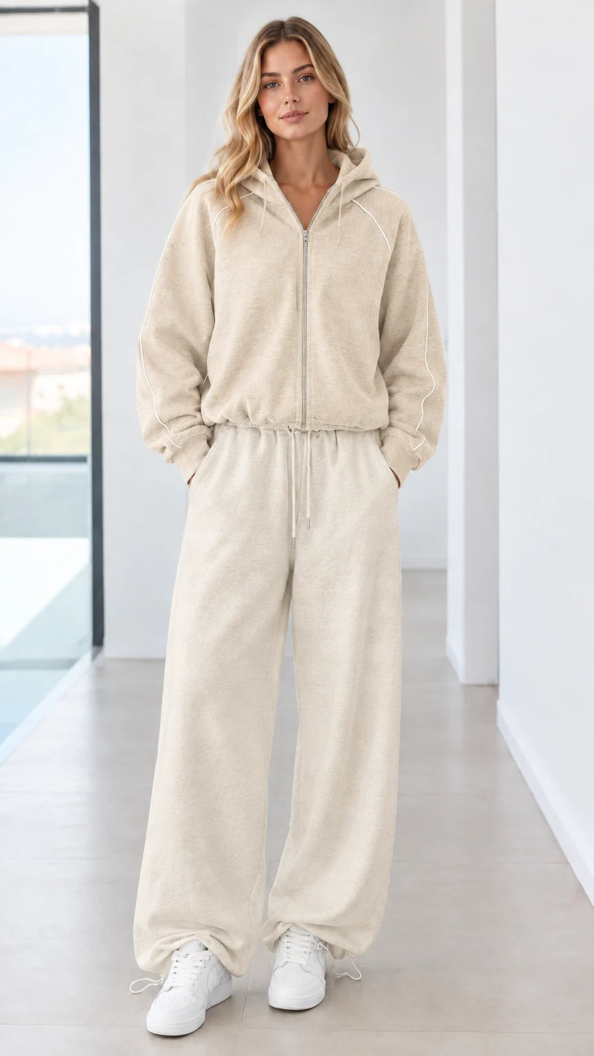 Full body studio shot of model wearing beige cream zip-up hoodie and wide-leg sweatpants set