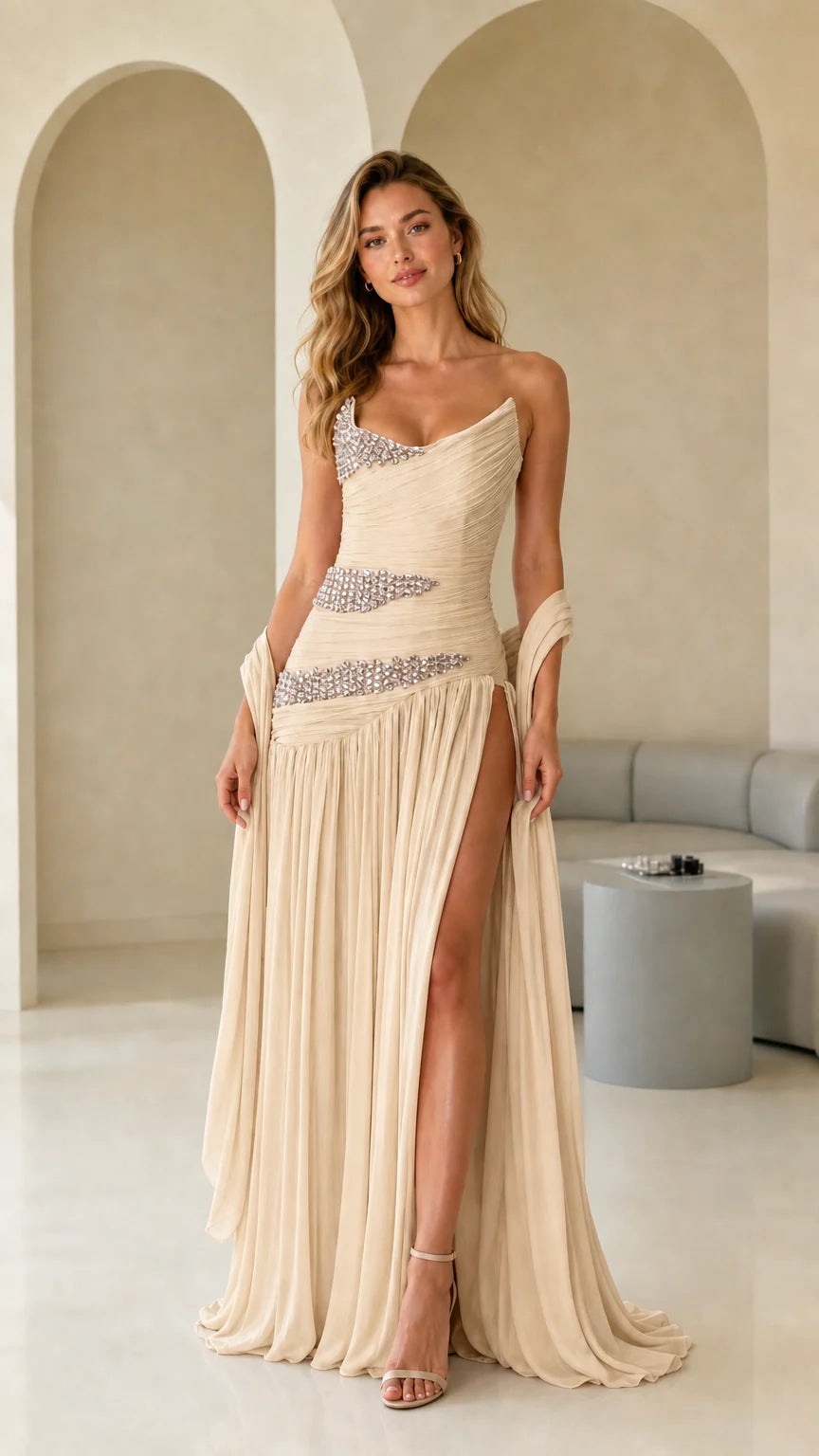 Model wearing champagne beige one-shoulder pleated maxi gown with rhinestone details